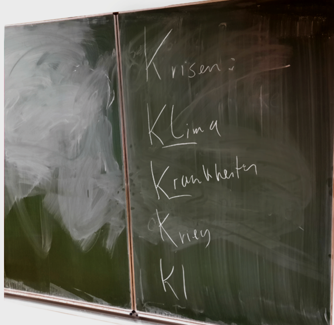 A classroom blackboard listing Krisen, Klima, Krankheiten, Krieg and KI